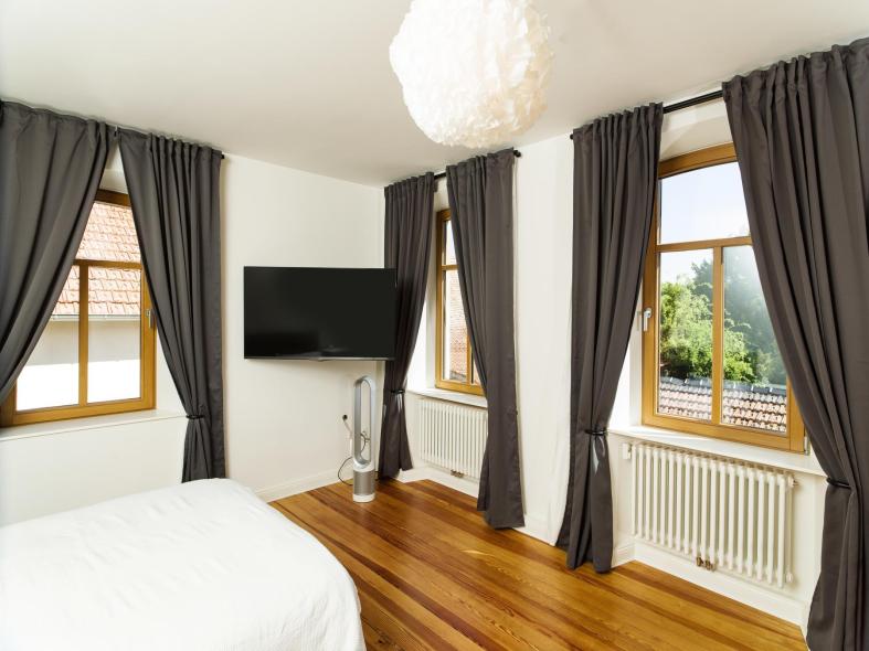 Schlafzimmer mit Holzboden und schwarzen Vorhängen vor den neuen Holzfenstern von PaX
